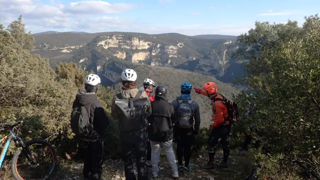 Un groupe de personne descendu de leur VTT pour observer la vue sur des montagnes et écouter les indications d'un animateur