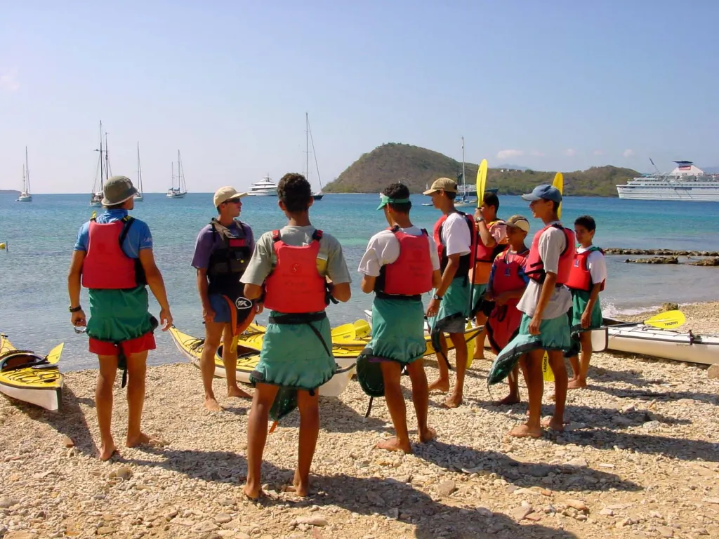 Groupe de personnes debout sur la plage écoutant attentivement les indications d'un animateur avant de faire une sortie kayak de mer