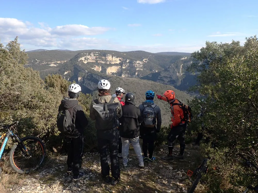 Un groupe de personne descendu de leur VTT pour observer la vue sur des montagnes et écouter les indications d'un animateur