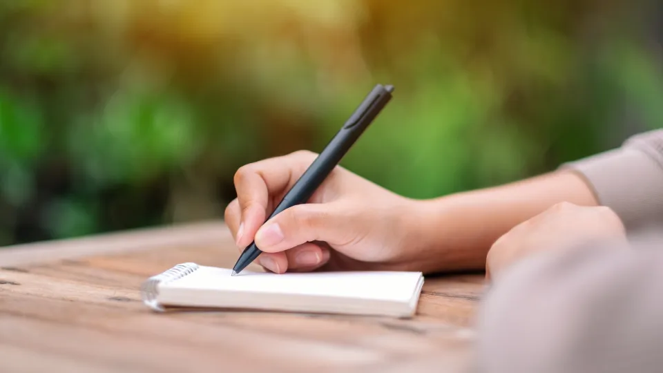 Une femme écrit avec stylo sur un calepin blanc